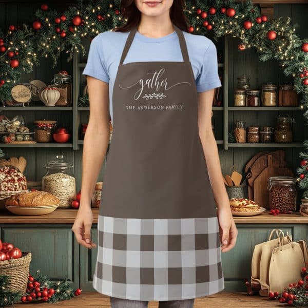 Brown Apron With A White And Brown Buffalo Plaid Bottom And The Words Gather The Anderson Family In A Script Font.