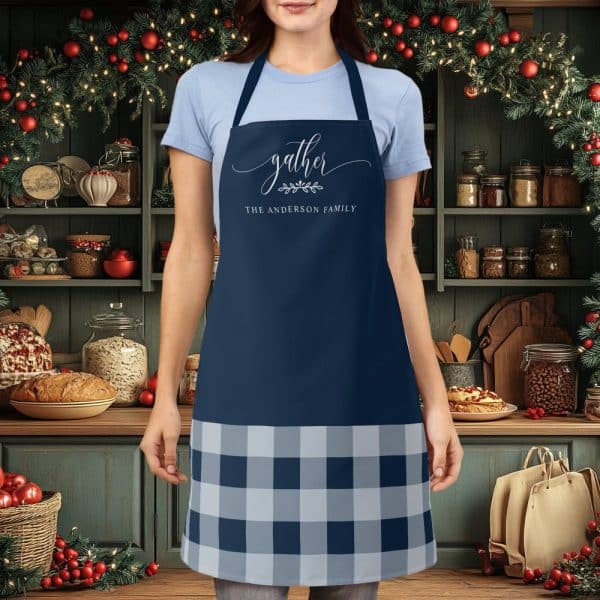 Person Wearing A Navy Blue Apron With A Gray And Navy Buffalo Plaid Bottom And The Words Gather, The Anderson Family On The Top.
