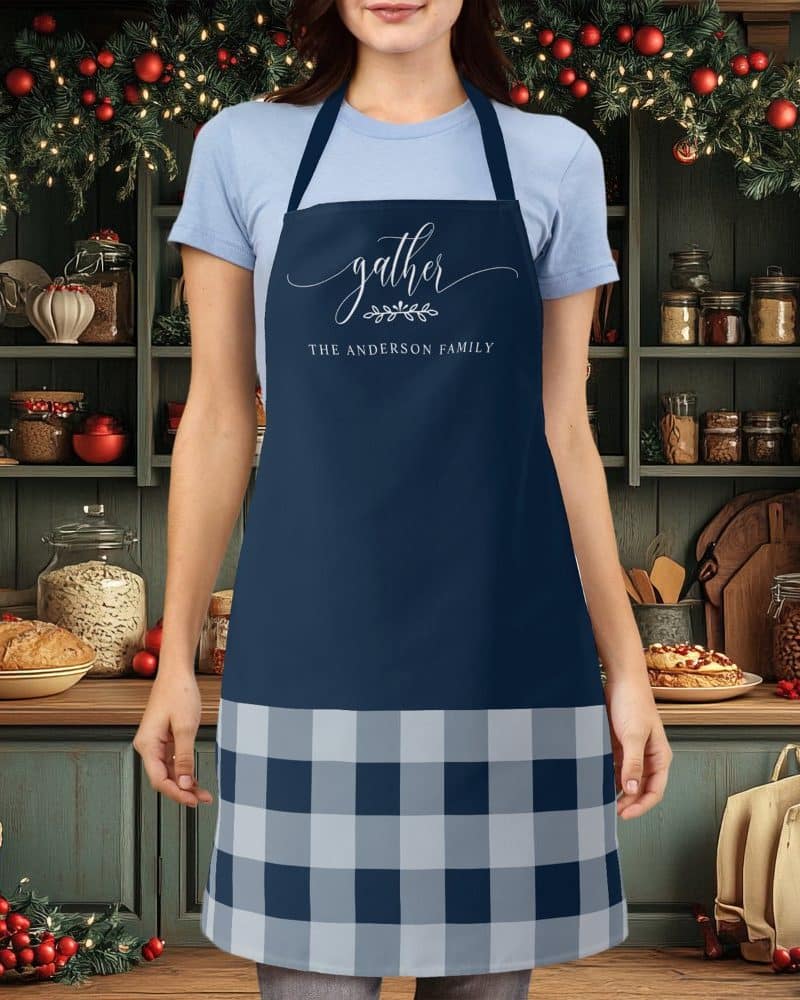 Person wearing a navy blue apron with a gray and navy buffalo plaid bottom and the words Gather, The Anderson Family on the top.