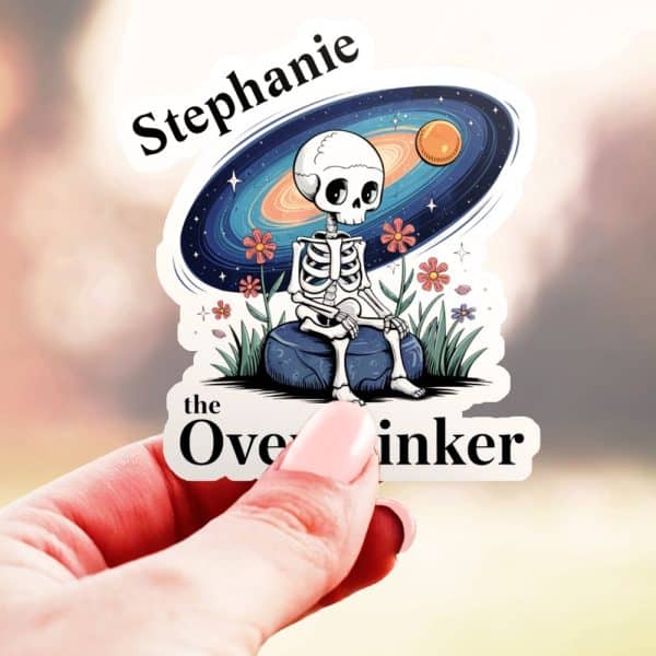 A Hand Holds A Sticker Featuring A Cartoon Skeleton Sitting On A Rock, Before A Galaxy Background. The Sticker Is Personalized With The Name Stephanie And The Words The Overthinker.
