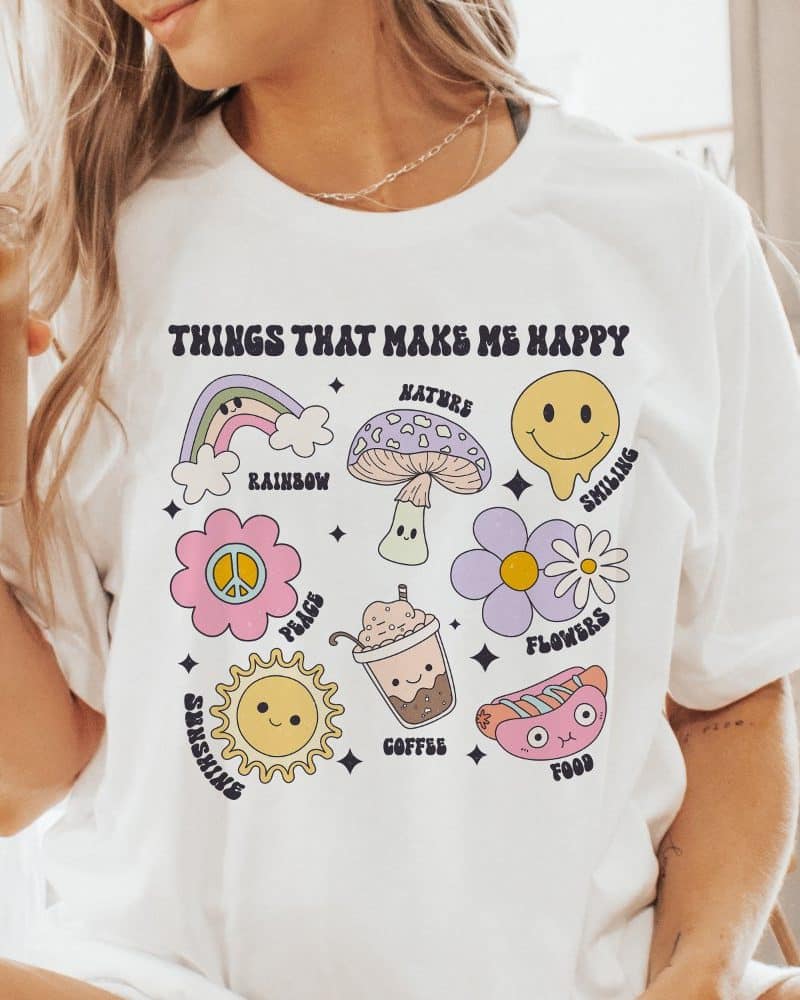 White t-shirt with illustrations of things that make people happy, including a rainbow, flowers, coffee, and sunshine.