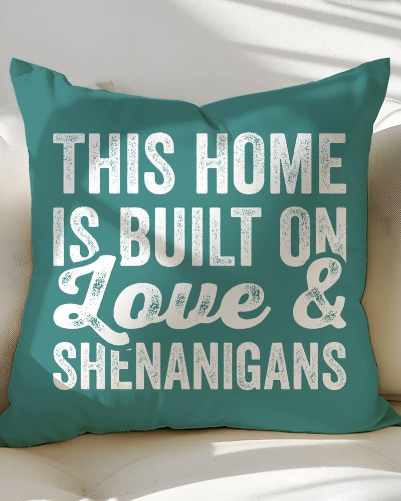 Teal throw pillow with white text reading This Home Is Built on Love & Shenanigans.