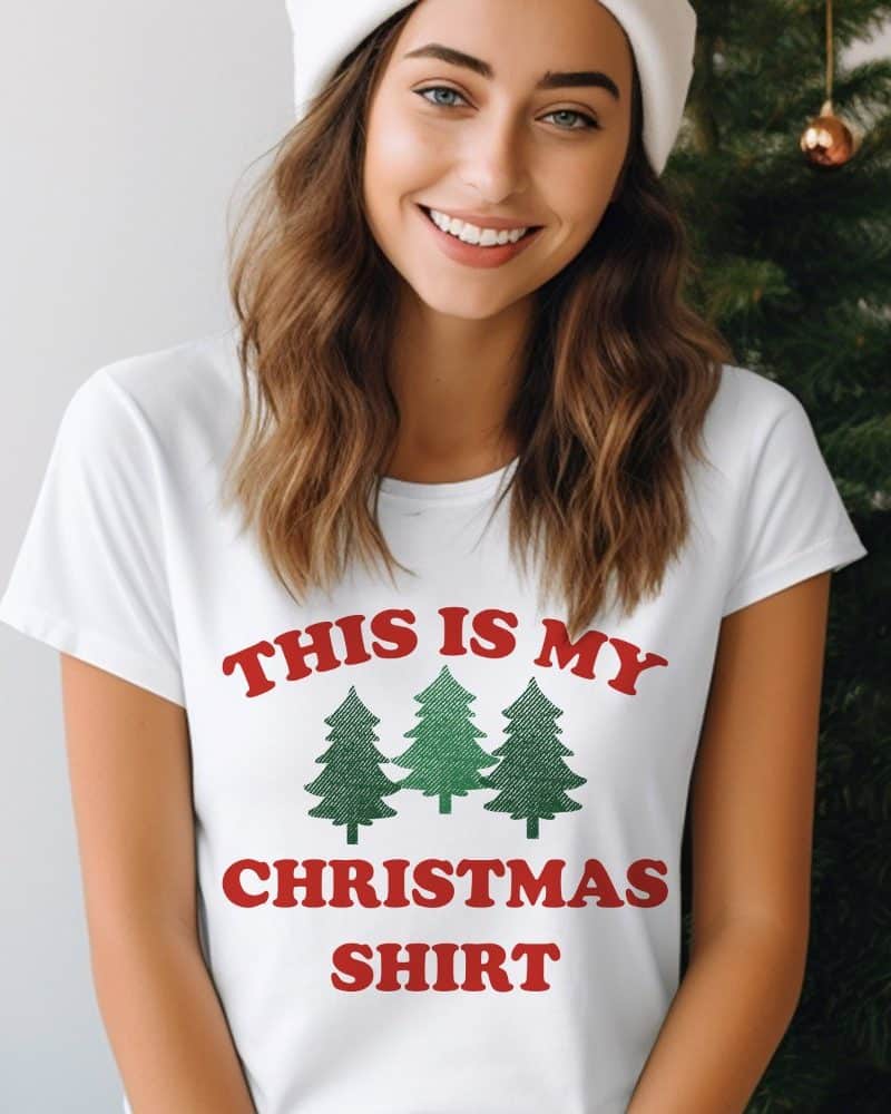 Woman wearing a white t-shirt with red text that says This Is My Christmas Shirt and a green graphic of three Christmas trees.