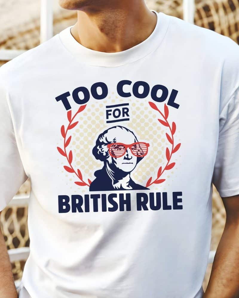 White t-shirt with a graphic of George Washington wearing shutter shades, surrounded by a laurel wreath, and text that reads "Too Cool For British Rule".