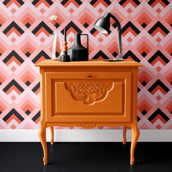 Orange Painted Wooden Cabinet With Ornate Detailing, Holding A Desk Lamp And Decorative Items.