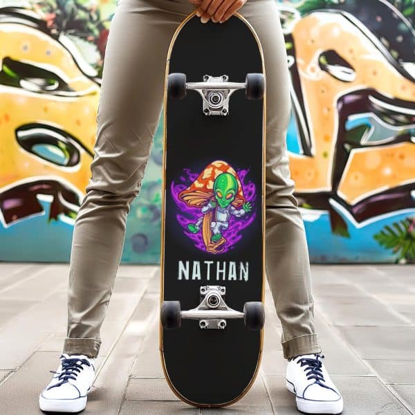 Person Holding A Black Skateboard With A Design Of An Alien On A Mushroom, And The Name Nathan.