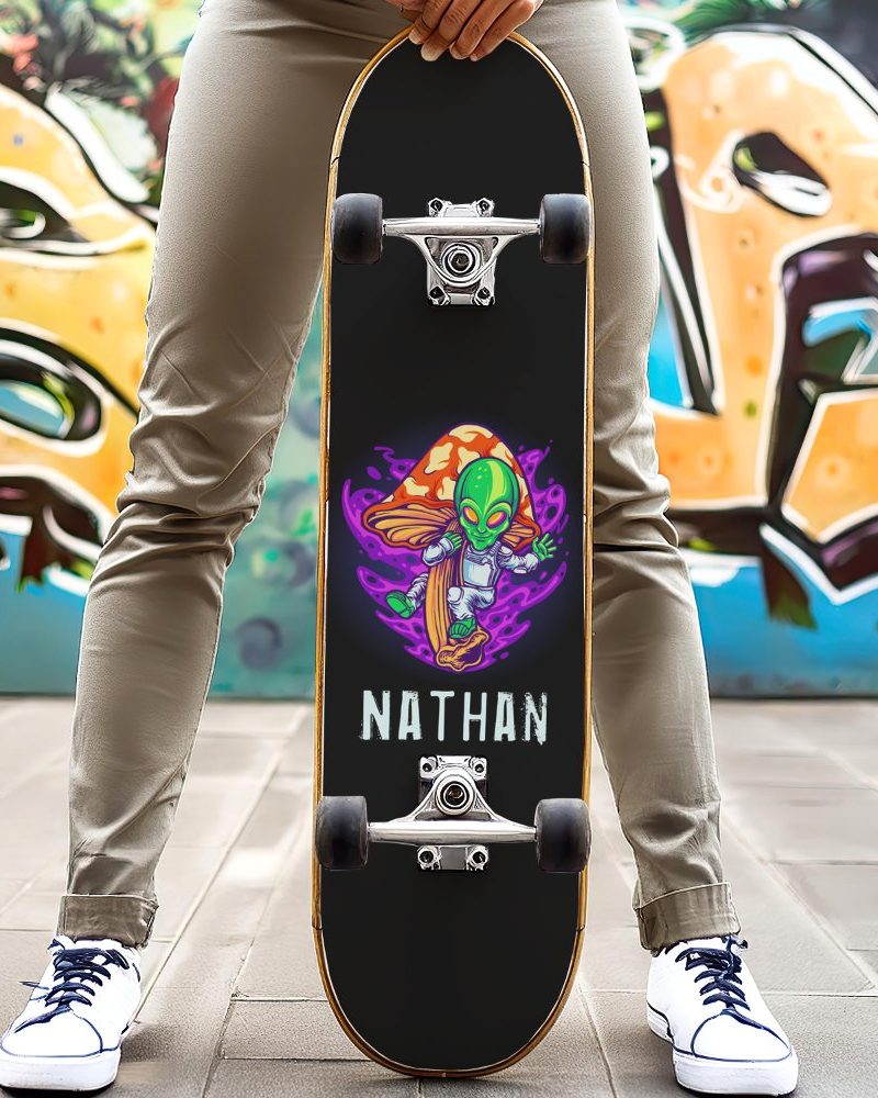 Person holding a black skateboard with a design of an alien on a mushroom, and the name Nathan.