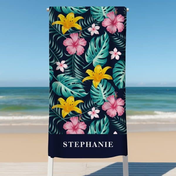 Personalized Beach Towel With A Tropical Floral Pattern, Featuring Lilies, Hibiscus Flowers, And Monstera Leaves On A Navy Background. The Name Stephanie Is Printed At The Bottom.