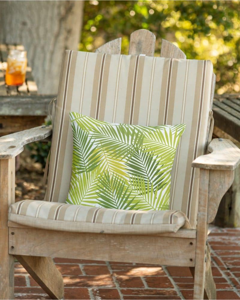 A green palm leaf patterned throw pillow sits on a wooden chair.