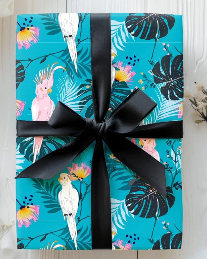 A teal gift box with a black ribbon, decorated with pink and white cockatoos and tropical leaves.