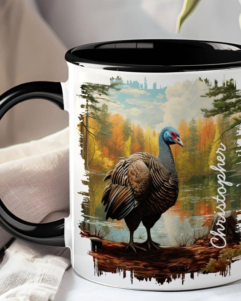 Black-handled mug with a painting of a wild turkey standing by a lake in an autumn forest.