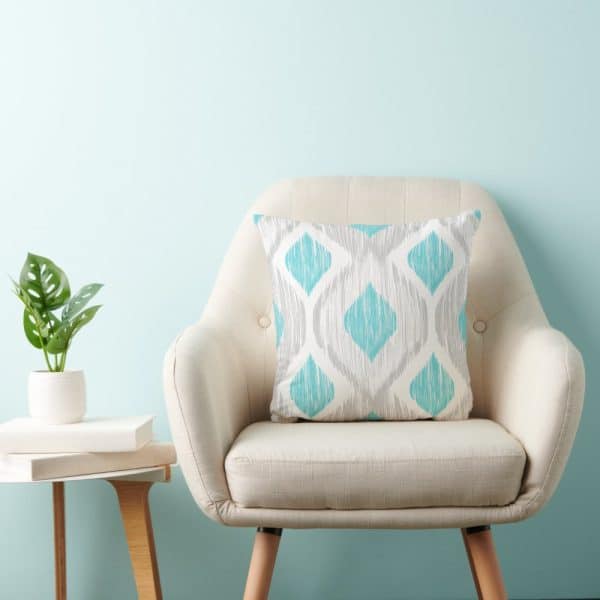Beige Armchair With A Teal And Gray Patterned Throw Pillow.