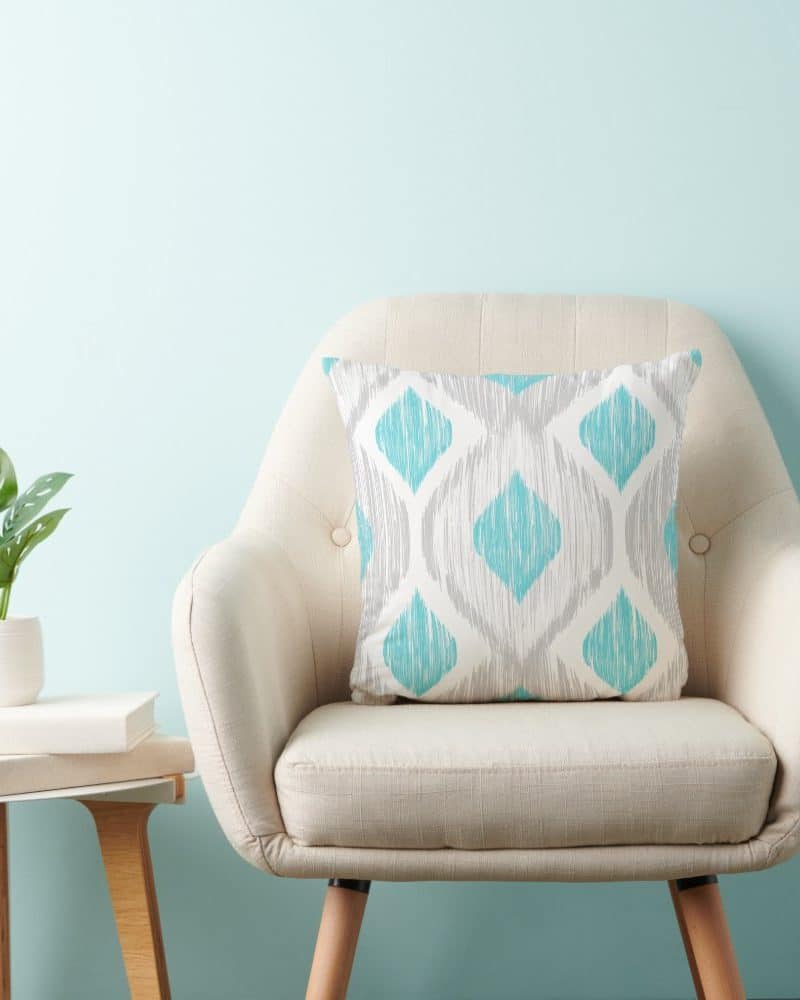 Beige armchair with a teal and gray patterned throw pillow.