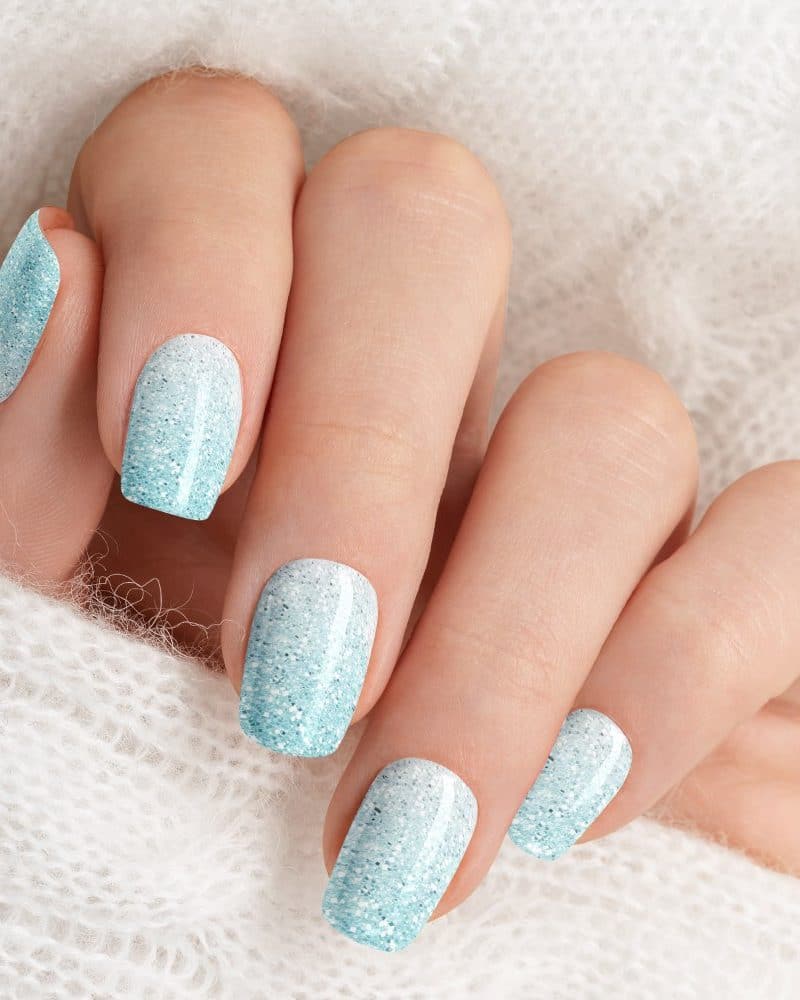 Closeup of a hand with light blue glitter ombre nail polish.