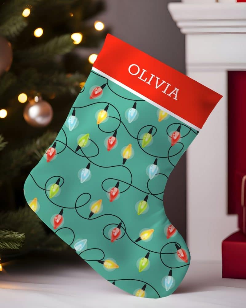 Teal Christmas stocking with a red cuff, personalized with the name Olivia, and decorated with a pattern of colorful string lights.