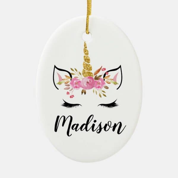 Oval Ceramic Christmas Ornament Featuring A Unicorn Face With Pink Flowers And A Gold Glitter Horn, Personalized With The Name Madison.
