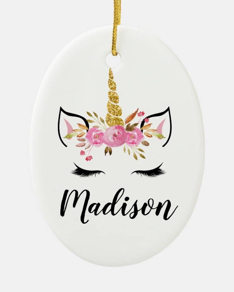 Oval ceramic Christmas ornament featuring a unicorn face with pink flowers and a gold glitter horn, personalized with the name Madison.