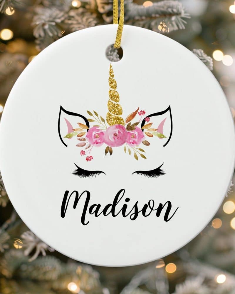 Round white Christmas ornament featuring a unicorn face with pink flowers and gold glitter horn, personalized with the name Madison.