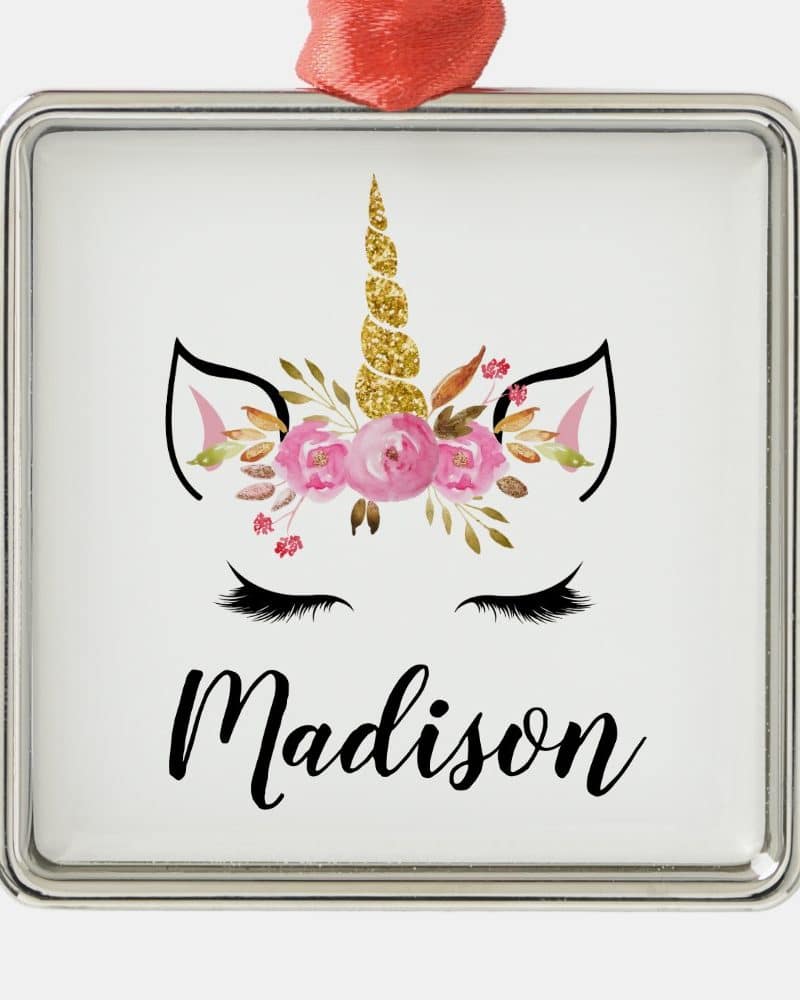 Silver square ornament featuring a unicorn face with a gold glitter horn and pink flowers, the name Madison below.