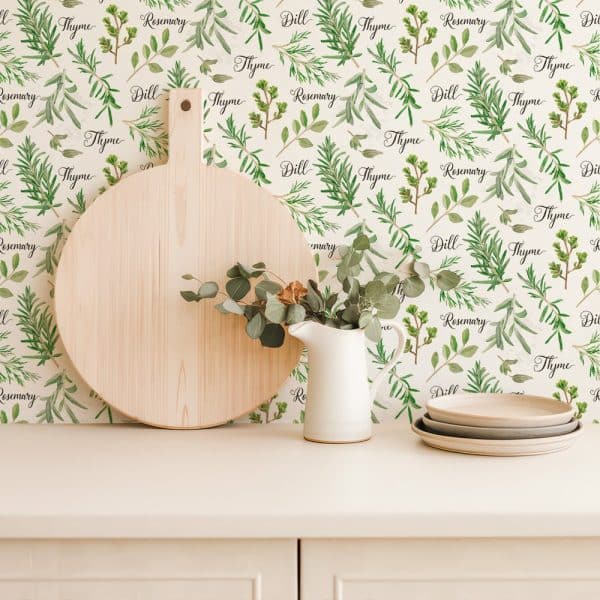 A Kitchen Counter With A Wooden Cutting Board, A White Creamer, And Stacked Plates Against A Backdrop Of Herb-Themed Wallpaper.