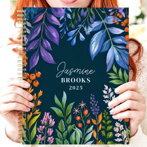 Person Holding A 2025 Spiral-Bound Planner With A Floral Design And Their Name, Jasmine Brooks.