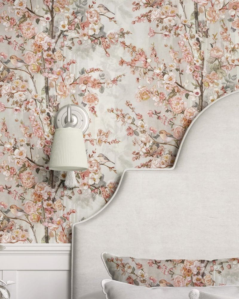 Floral wallpaper featuring pink blossoms, branches, and small birds, partially visible behind a light-grey headboard.
