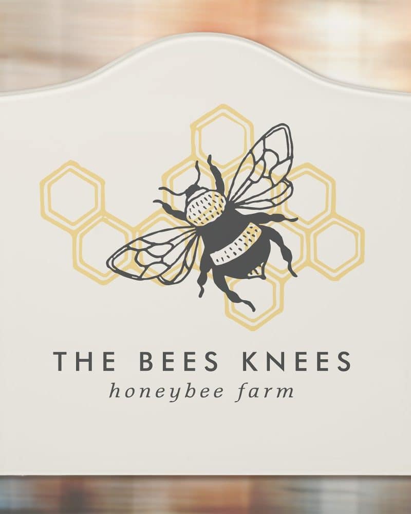 A cream-colored sign featuring a black bumblebee on a honeycomb design, with the text "The Bees Knees honeybee farm" below.