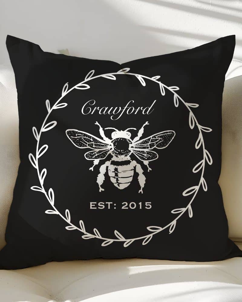 Black pillow with a white bee illustration in a wreath design, the name Crawford and the year 2015.