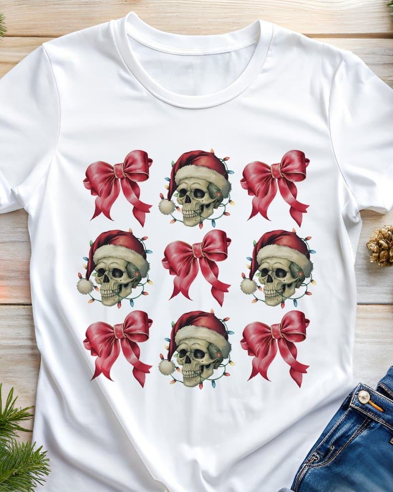 White t-shirt with a repeating pattern of skulls wearing Santa hats and surrounded by Christmas lights and red bows.