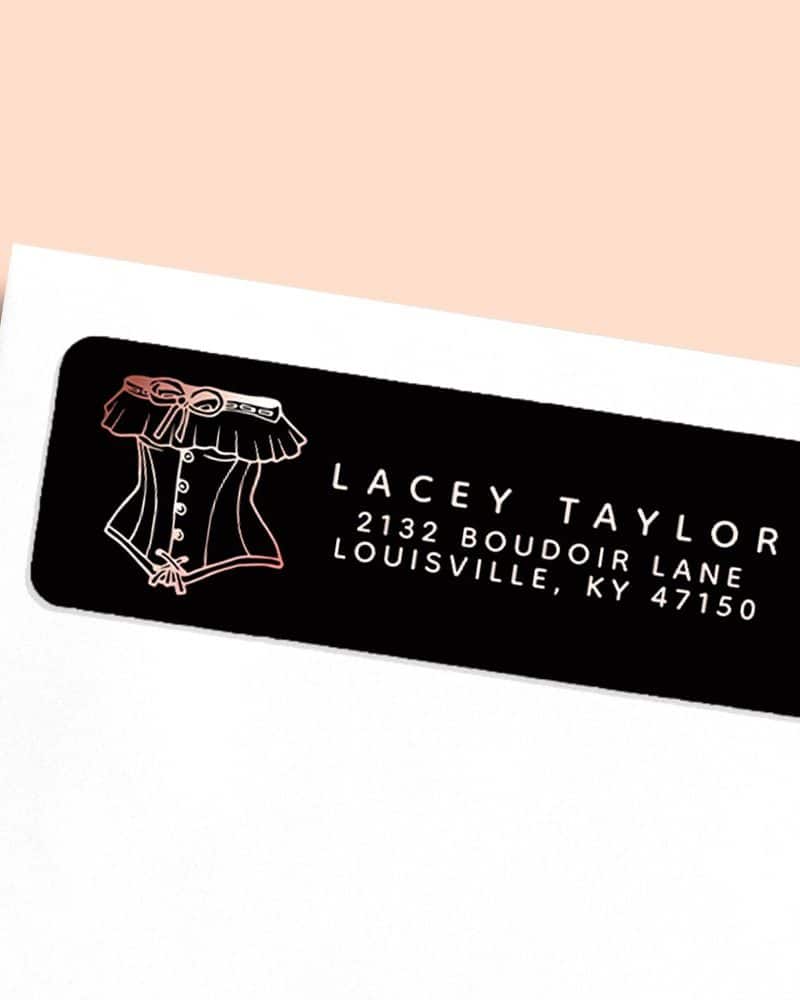 Black return address label with a rose gold corset illustration and white lettering.