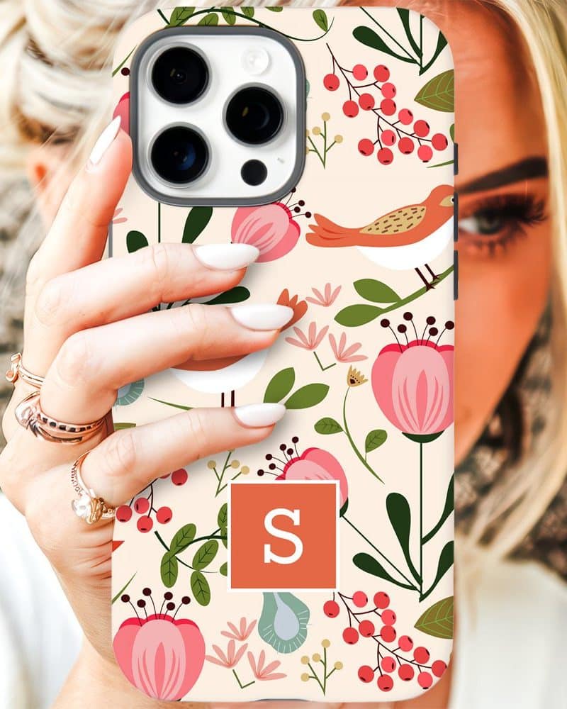 A woman's hand holding up an iPhone case with a floral and bird pattern, and the initial S in a coral square.