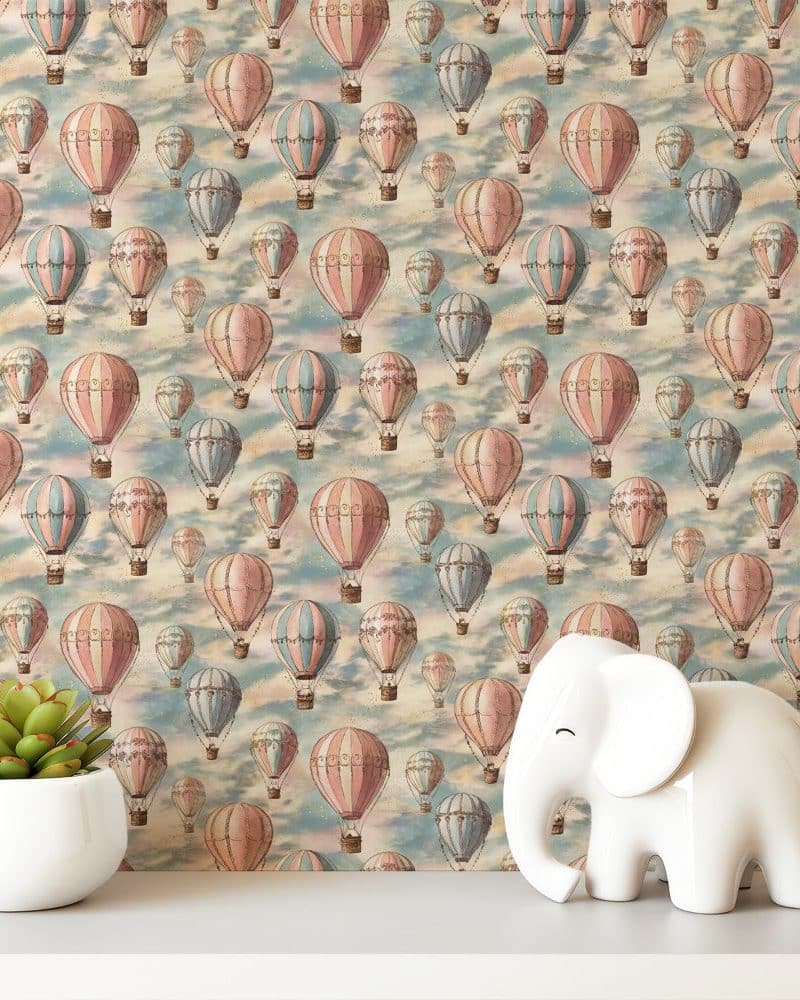 White elephant figurine in front of wallpaper featuring a repeating pattern of pastel hot air balloons.