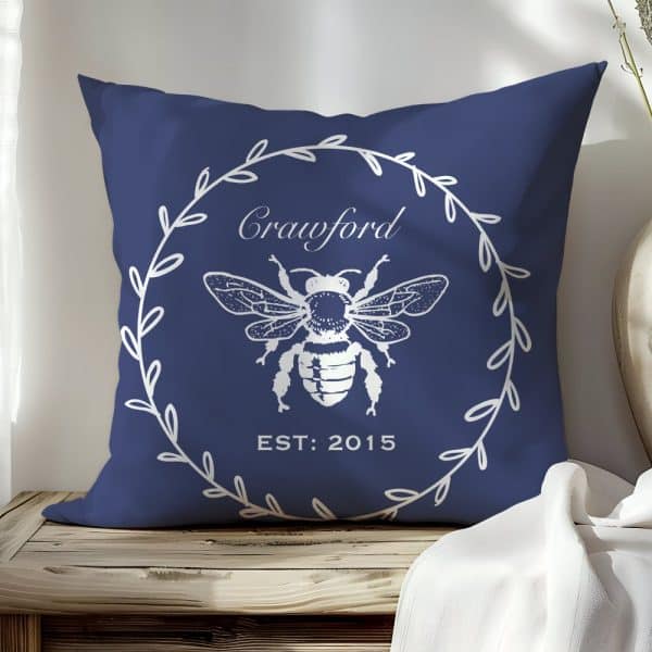 Navy Blue Throw Pillow With A White Bee Illustration, Wreath, And The Name Crawford.