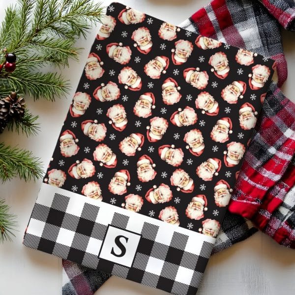A Black And White Buffalo Plaid Christmas Gift Wrap Featuring A Repeating Pattern Of Santa Claus Faces And Snowflakes. A Monogrammed Initial S Is In The Center Of The Plaid Bottom.