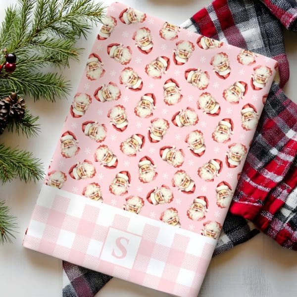 Pink Wrapping Paper With A Repeating Pattern Of Vintage Santa Claus Faces And Snowflakes. A Pink And White Gingham Border Features A White Letter S.