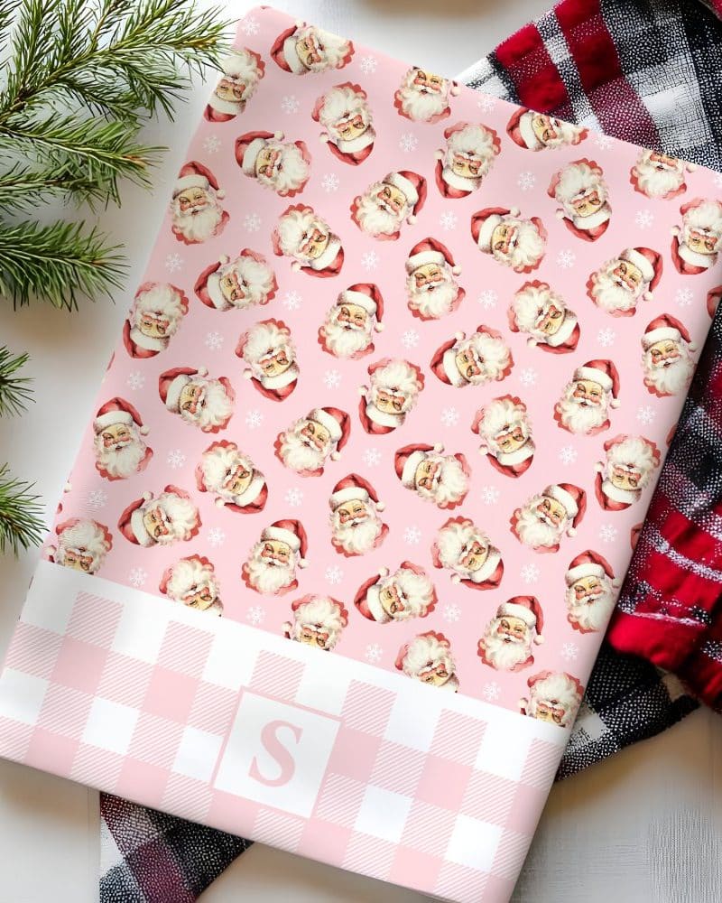 Pink wrapping paper with a repeating pattern of vintage Santa Claus faces and snowflakes. A pink and white gingham border features a white letter S.