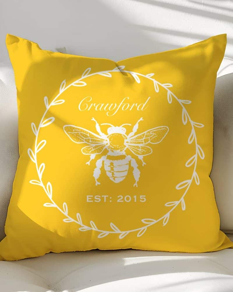 Yellow throw pillow with a white bee illustration, wreath, and the text Crawford Est 2015.