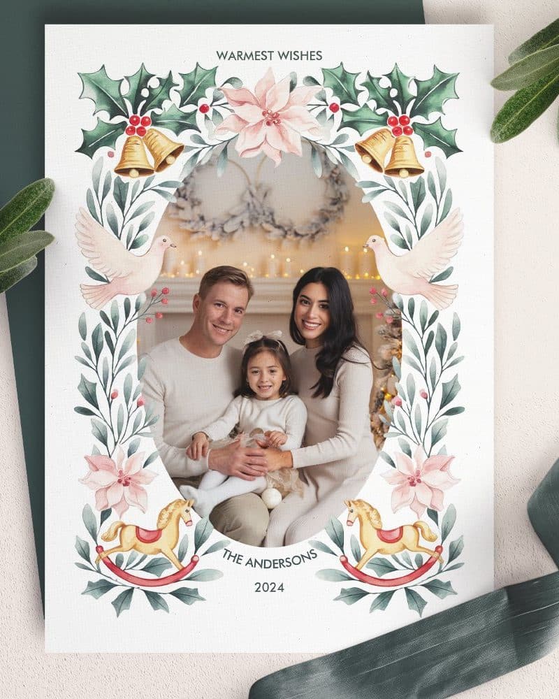 Christmas card featuring a family portrait framed by a watercolor floral design with doves, bells, and rocking horses.