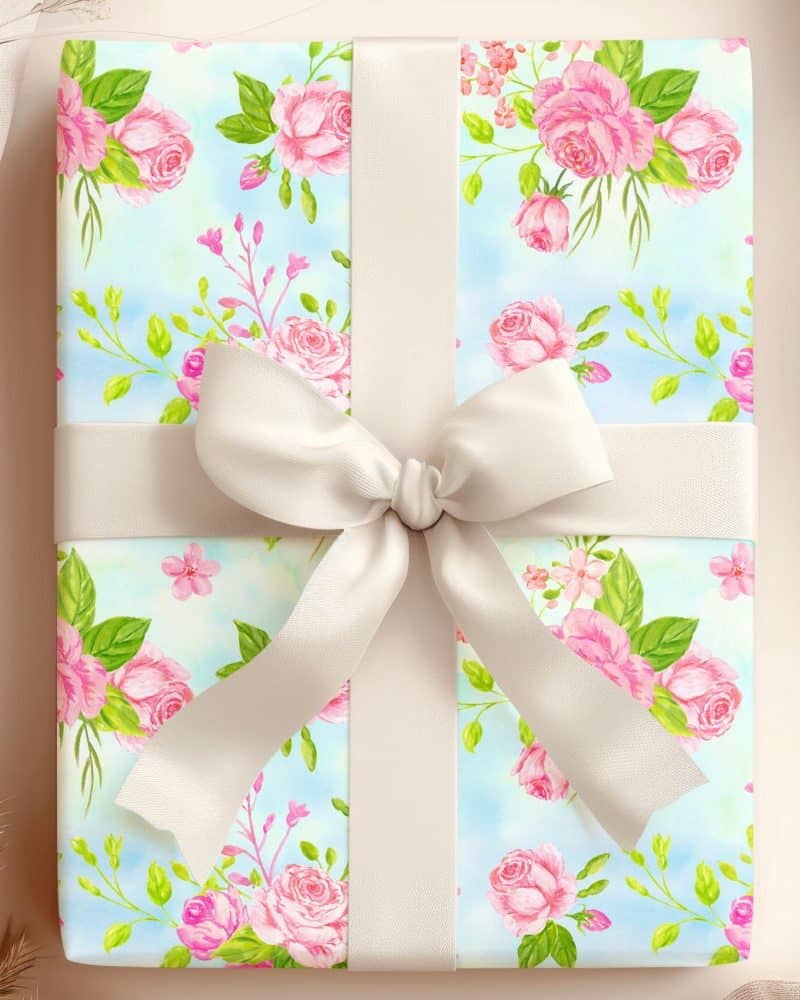 A gift wrapped in light blue paper with a pink rose pattern and tied with a large cream-colored bow.