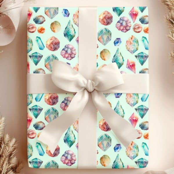A Gift Wrapped In Light Green Paper Featuring A Watercolor Pattern Of Colorful Gemstones And Crystals, Tied With A Cream-Colored Ribbon.