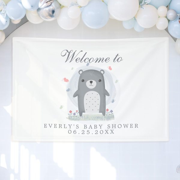 White Baby Shower Banner Featuring A Cute Cartoon Bear Surrounded By Flowers And Butterflies. The Banner Also Includes The Baby'S Name And Shower Date.