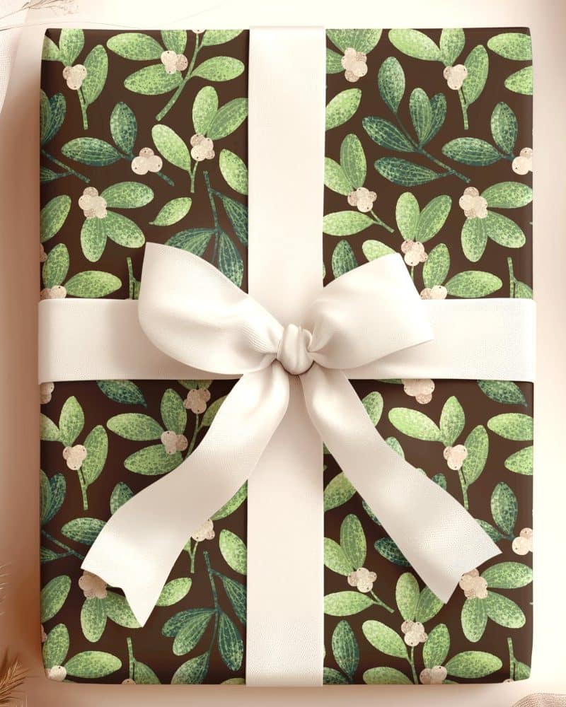 A gift wrapped in brown paper with a green mistletoe pattern and tied with a cream-colored ribbon.