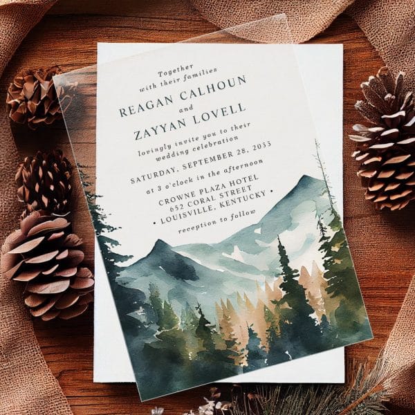 Clear Wedding Invitation With Watercolor Mountain And Forest Scene. The Invitation Features The Names Reagan Calhoun And Zayyan Lovell.