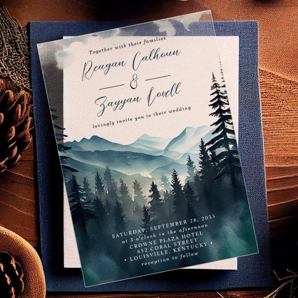 Clear Wedding Invitation With Watercolor Painting Of Mountains And Pine Trees. The Names Reagan Calhoun And Zayyan Lovell Are Prominently Displayed.