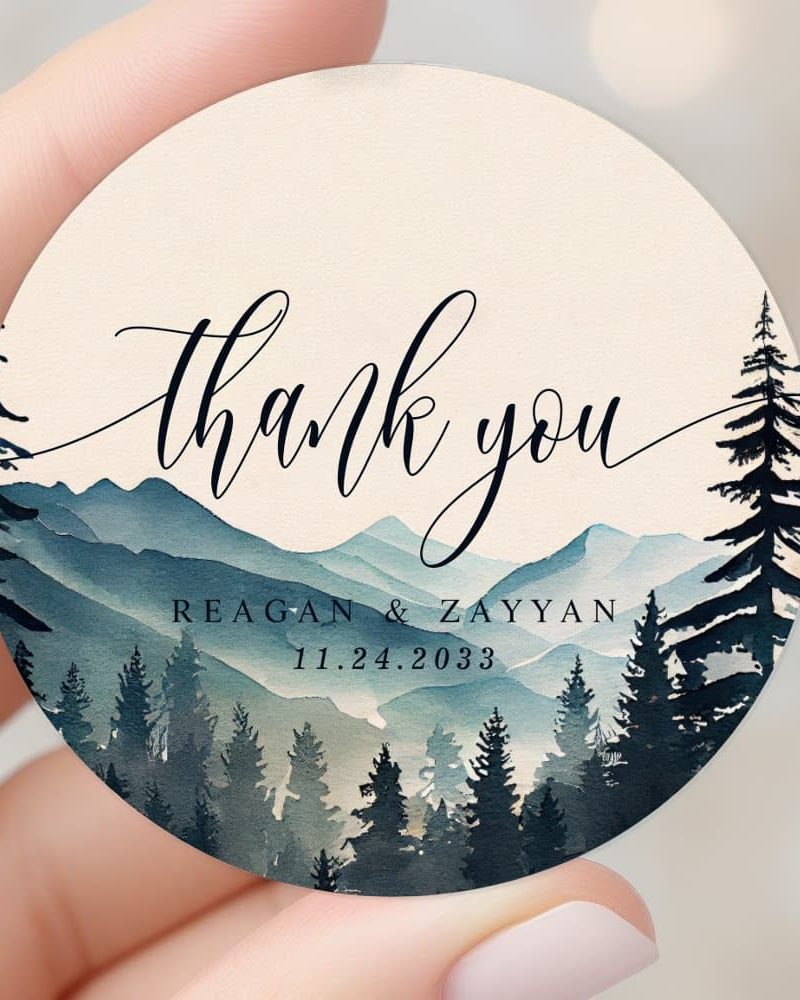 Round thank you sticker with watercolor mountains and forest scene. Reagan & Zayyan wedding date 11.24.2033.
