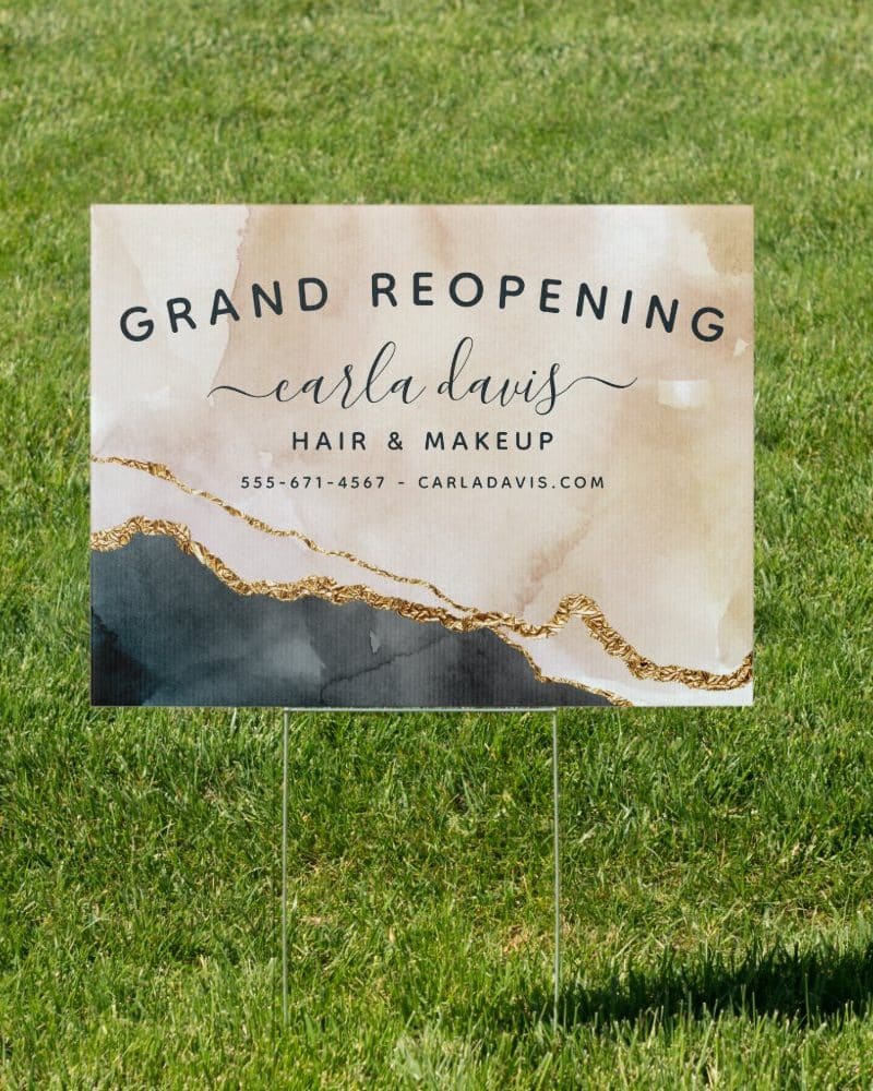 Grand reopening announcement for Carla Davis Hair & Makeup, displayed on a yard sign with an abstract design.