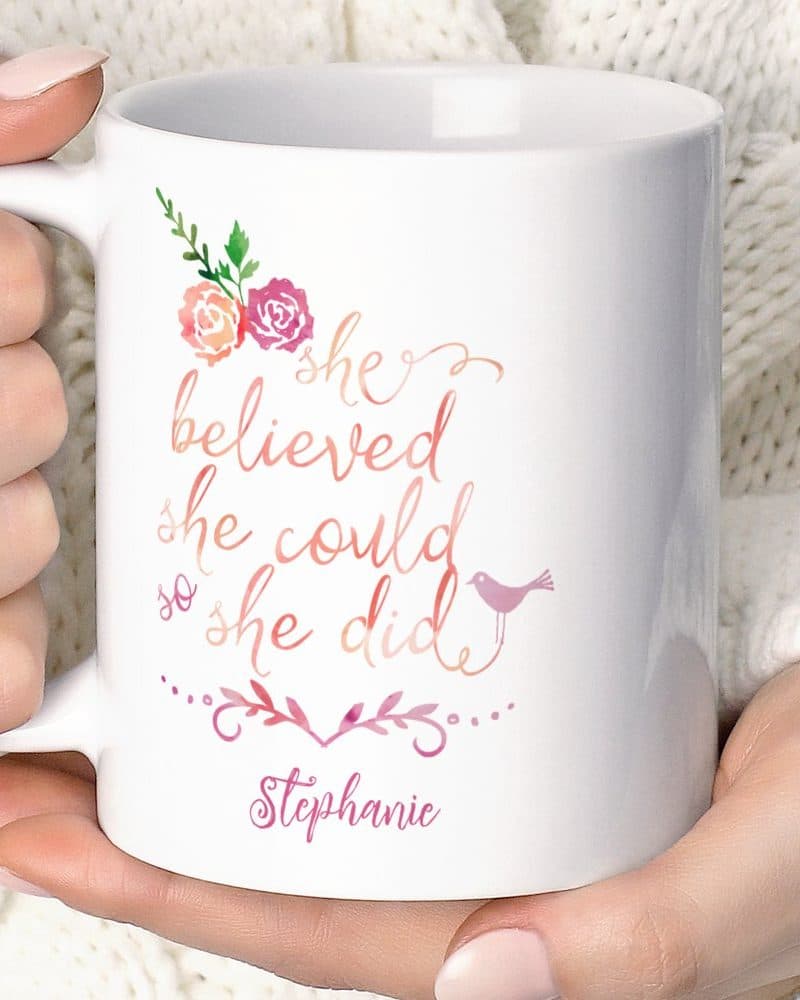 A white coffee mug with the inspirational text She believed she could so she did, along with watercolor flowers, a bird, and the name Stephanie.