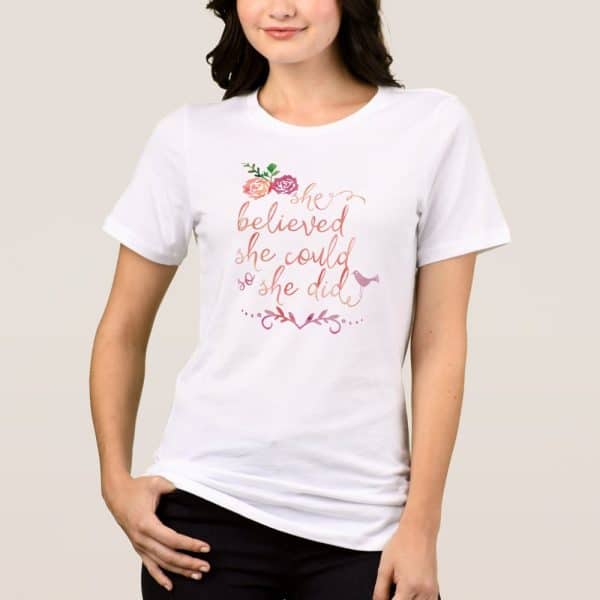 White T-Shirt Featuring The Text She Believed She Could So She Did, Adorned With Floral Accents And A Small Bird.