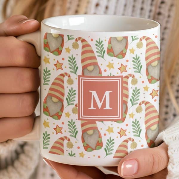 A White Coffee Mug With A Pattern Of Gnomes, Foliage, And Stars, And A Monogrammed Initial M In The Center.