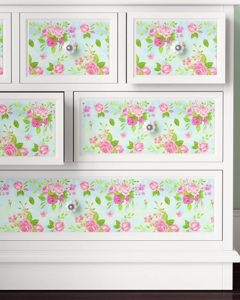 White dresser with drawers covered in pink rose floral wallpaper.